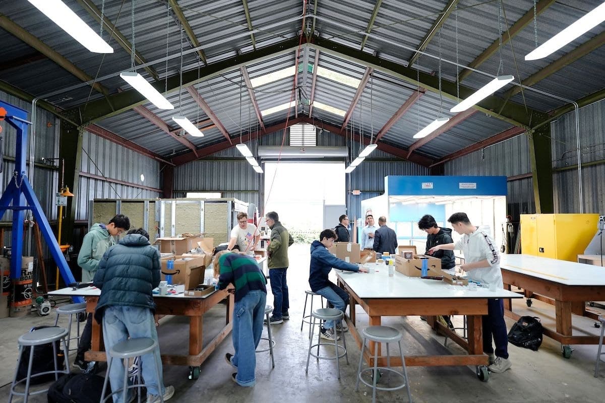 Workshop participants unpack drone kits and work together at long tables inside a fabrication space.